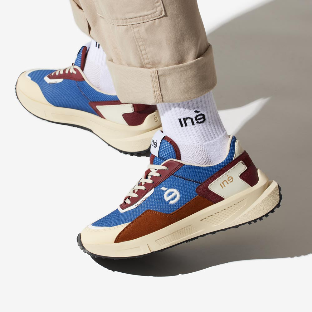 Baskets vegan bleu et camel unisexes de la marque iné, disponibles du 36 au 46 portées avec un pantalon beige