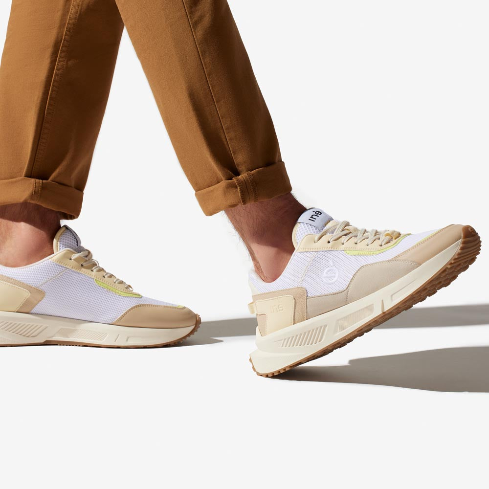 Homme portant des sneakers crème et jaune et un pantalon marron de la marque iné, disponibles du 36 au 46