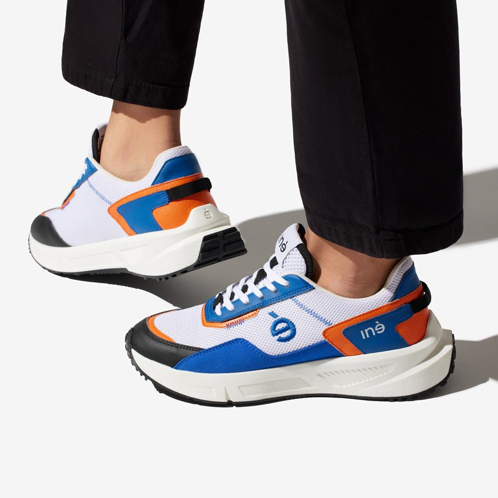 Sneakers vegan unisexes orange et bleu et jean noir de la marque iné,  disponibles du 36 au 46 portées avec un pantalon noir
