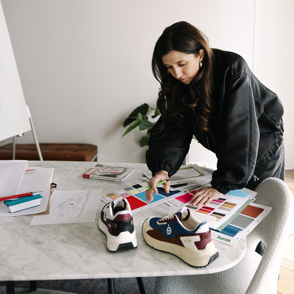 Audrey Delanoë, fondatrice d'iné, en train de travailler à l'aide de nuanciers et d'échantillons de tissu. Elle utilise 2 sneakers vegan et unisexes de sa collection Vibes ainsi qu'un dessin au crayon de papier pour créer.