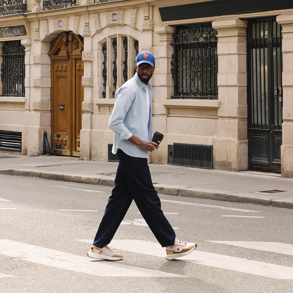 Homme traversant la rue avec un café et portant des sneakers beige et noir de la marque iné, baskets unisexes et vegan