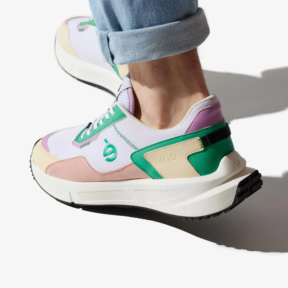 Une personne chaussée de sneakers mixtes, vegan de la marque iné. La paire est vert et rose