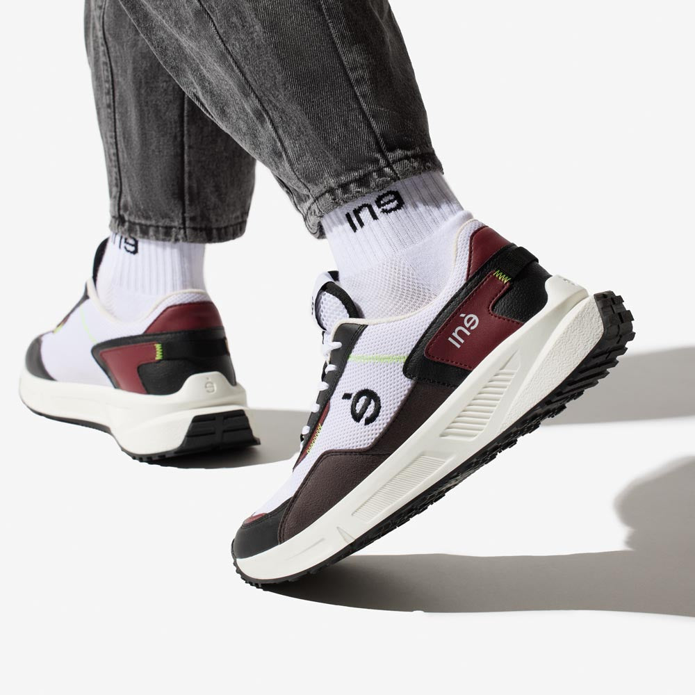 Personne portant des sneakers vegan unisexes bordeaux et noir de la marque iné, disponibles du 36 au 46 et un jean noir