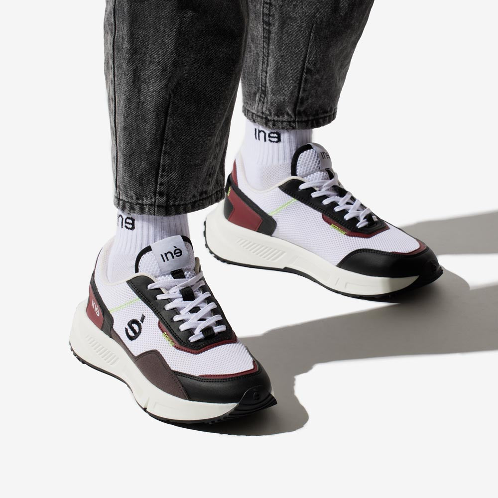 Personne portant des sneakers vegan unisexes bordeaux et noir de la marque iné, disponibles du 36 au 46 et un jean noir