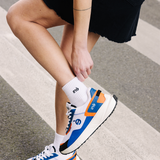 Femme portant des sneakers orange, ajustant sa chaussette "iné" de la marque iné, disponibles du 36 au 46