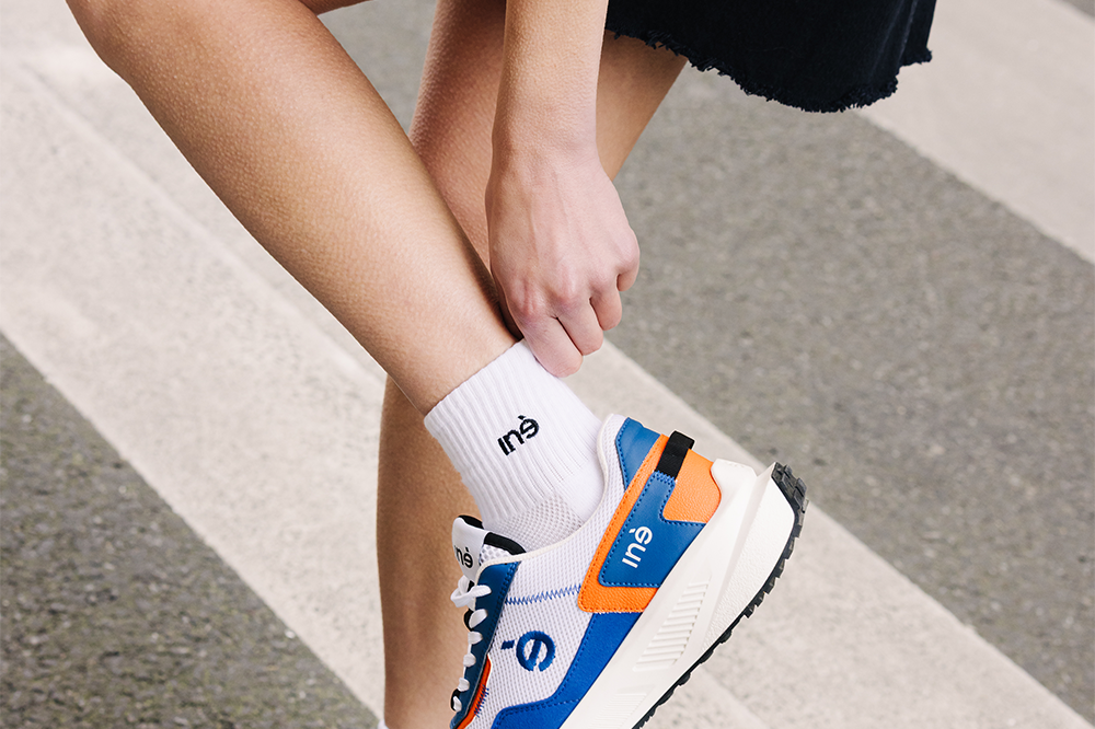 Femme portant des sneakers orange, ajustant sa chaussette "iné" de la marque iné, disponibles du 36 au 46